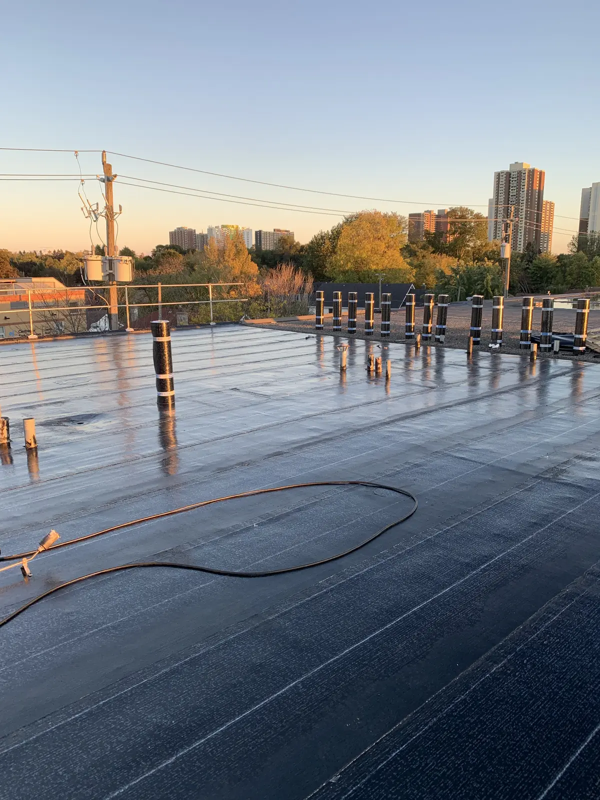 Freshly installed flat roof membrane at sunset, city towers behind: flat & commercial roofing by Eagle Roofing