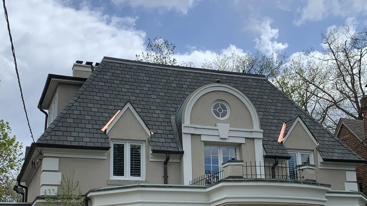 Synthetic slate roof with copper flashing on the dormers and a round window, a roof by Eagle Roofing